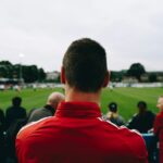 man standing while watching soccer during daytime